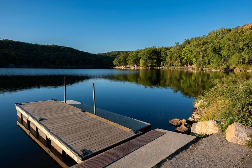 A wooden dock extending into calm water, surrounded by lush greenery and hills.