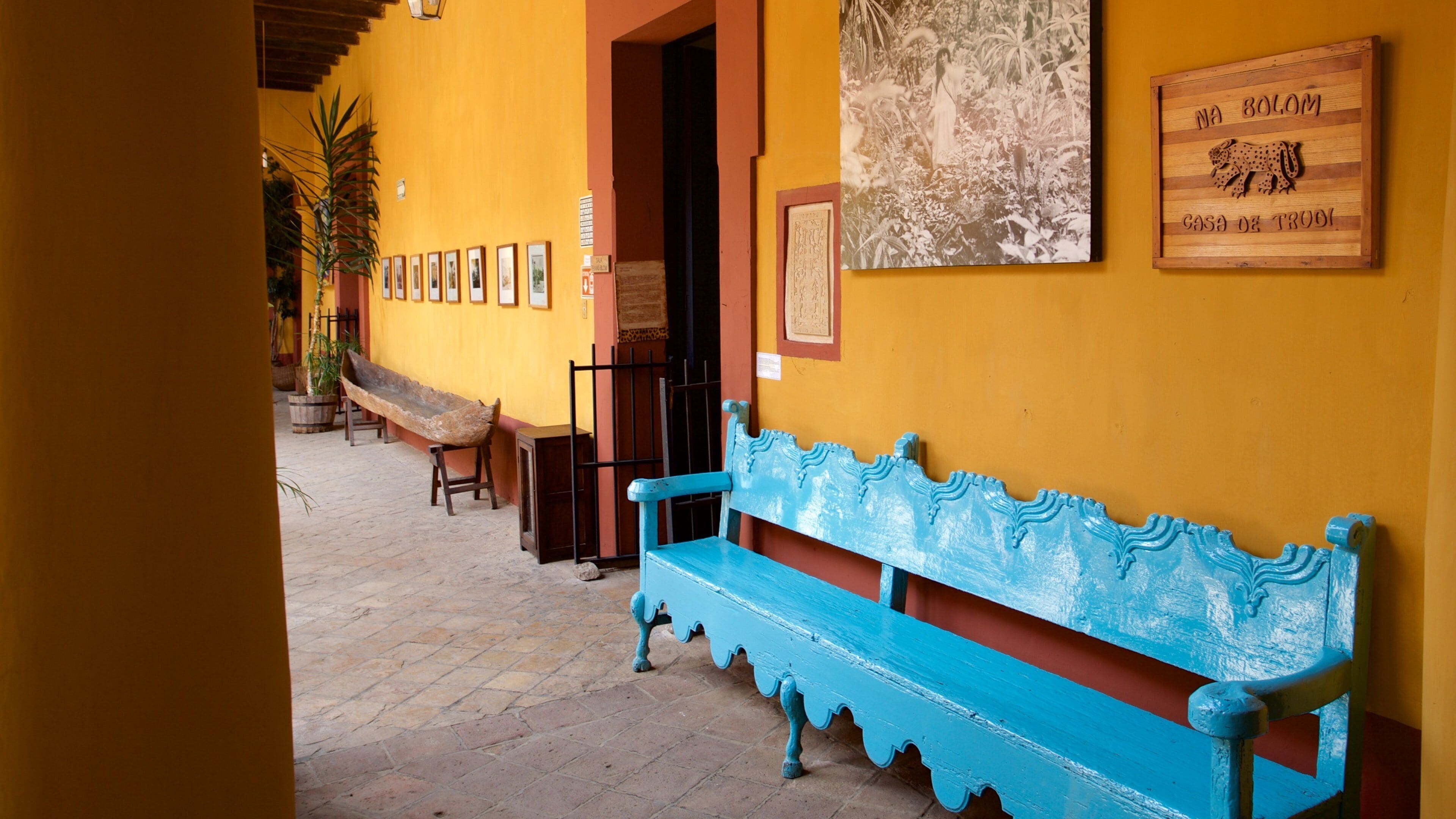 A courtyard with a blue bench, a wooden sculpture, and a wall with framed pictures.