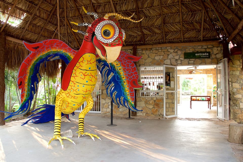 Una scultura di un uccello colorato in un ambiente esterno con tetto di paglia e pareti in pietra.