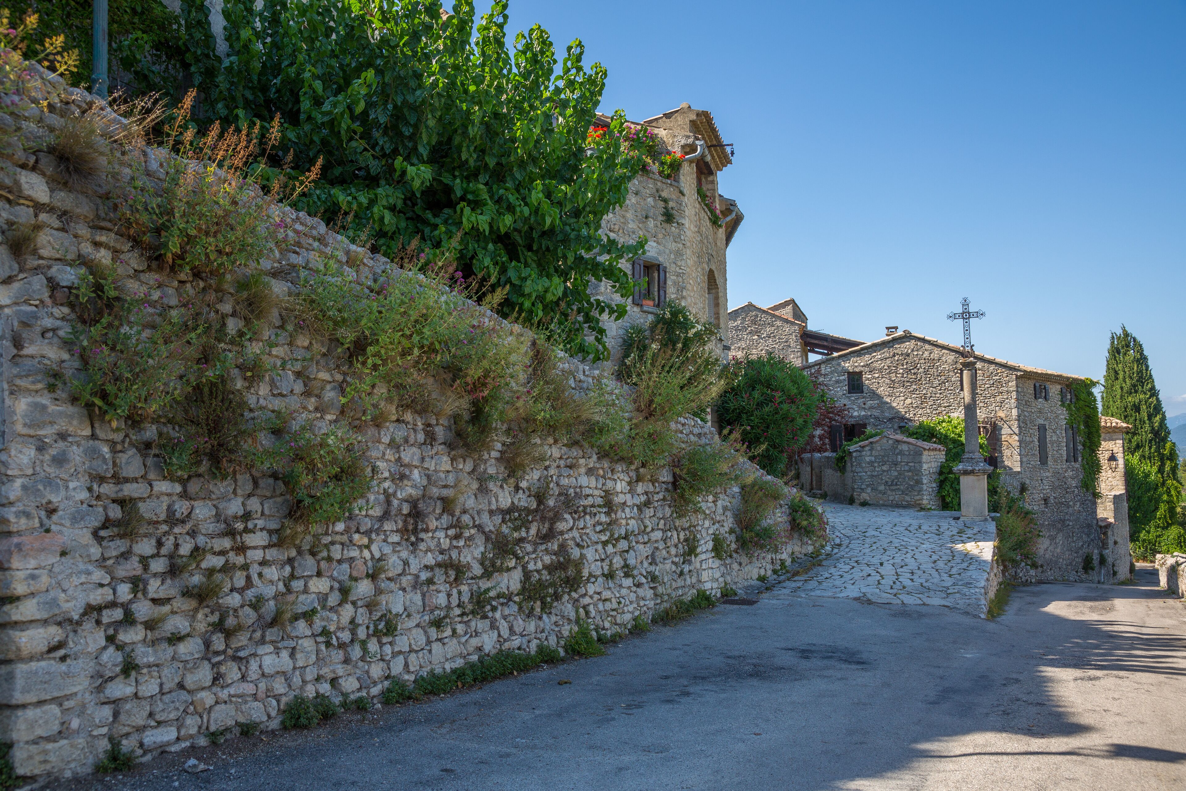 A stone wall with vegetation, a cobblestone path, and traditional stone buildings.