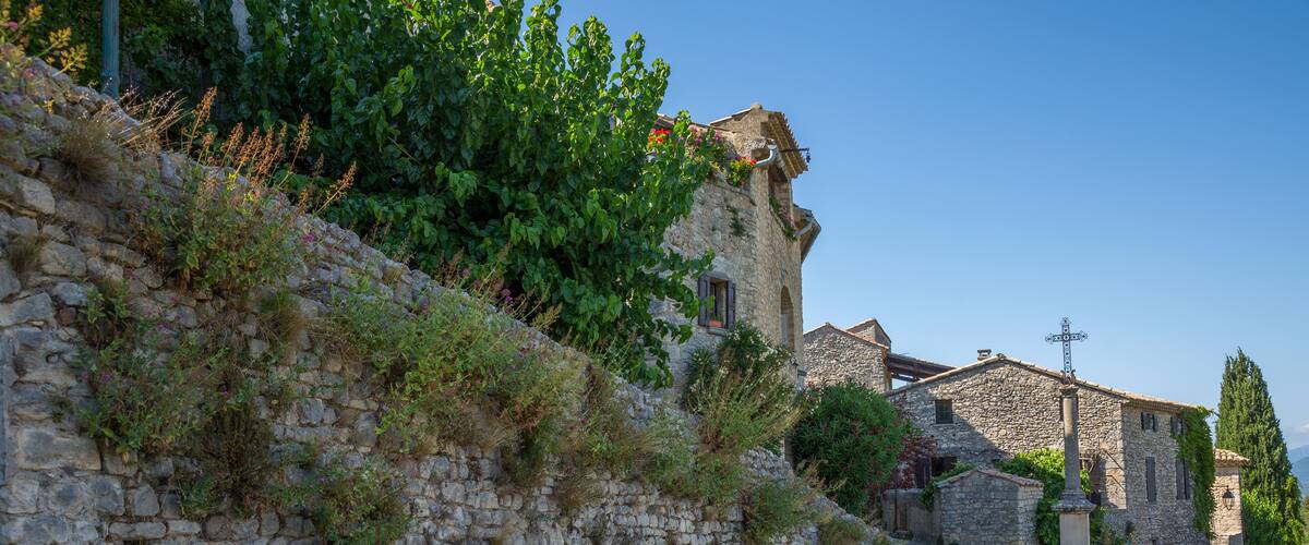 A stone wall with vegetation, a cobblestone path, and traditional stone buildings.