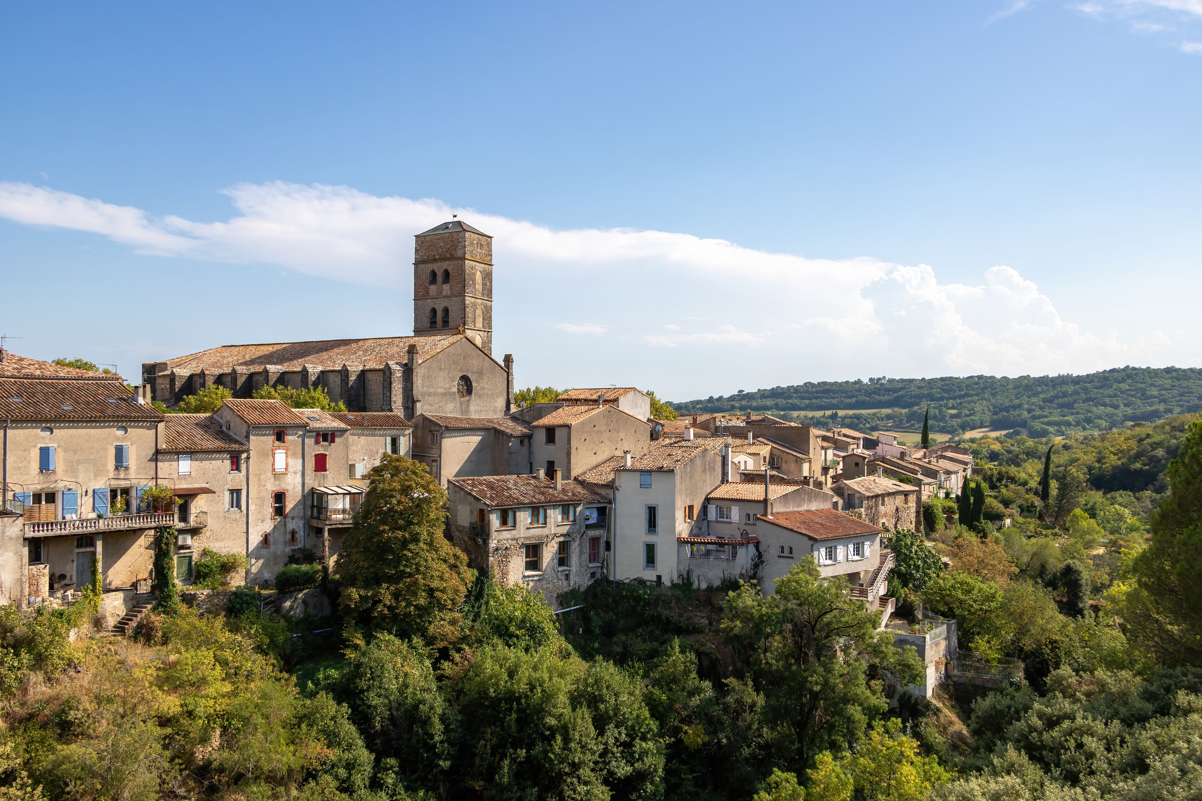 A view of the village of Montolieu Aude Languedoc - Roussillon France. Trees valley ancient houses and church bell tower.
