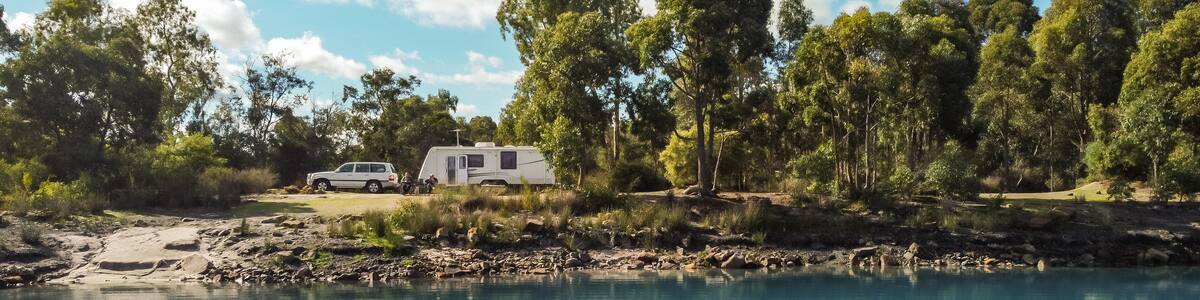 Landsscape view of a large modern caravan and four wheel drive vehicle free camping alongside a beautiful blue lake fringed with gumtrees.