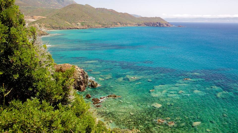 A coastal landscape with clear turquoise waters, rocky outcrops, and lush green vegetation.