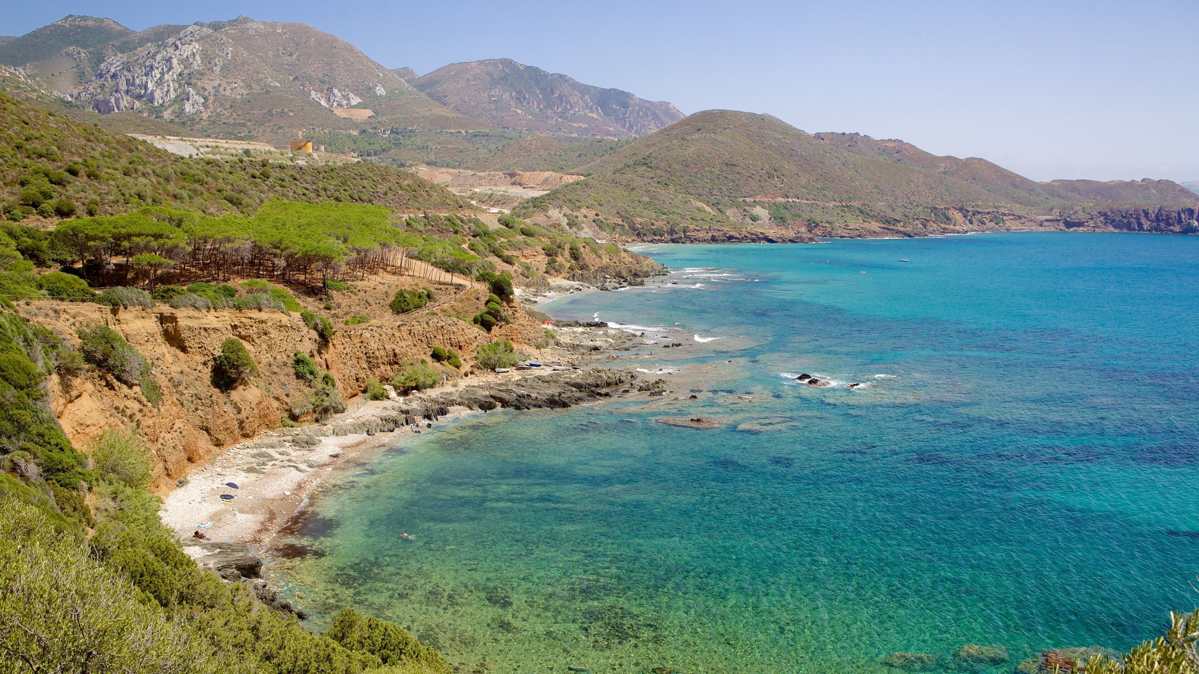 A coastal landscape with clear turquoise waters, rocky cliffs, and green vegetation.