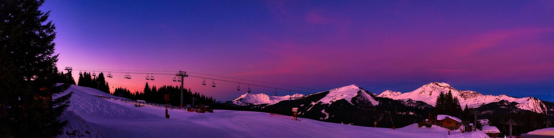 A snow-covered ski slope at dusk with a mountain in the background.