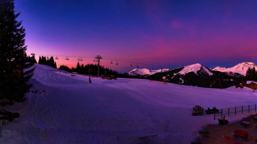 Une piste de ski enneigée au crépuscule, avec une montagne en arrière-plan.