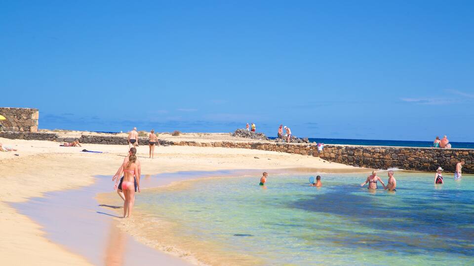 A beach with clear turquoise water, a stone wall, and people enjoying the sunny weather.