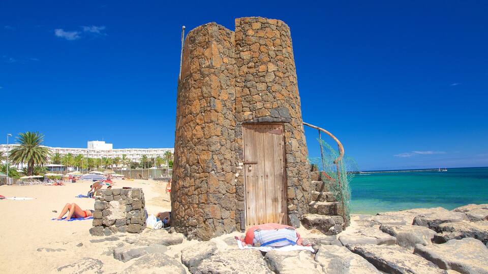 A stone tower on a beach with clear blue water and a few people sunbathing.