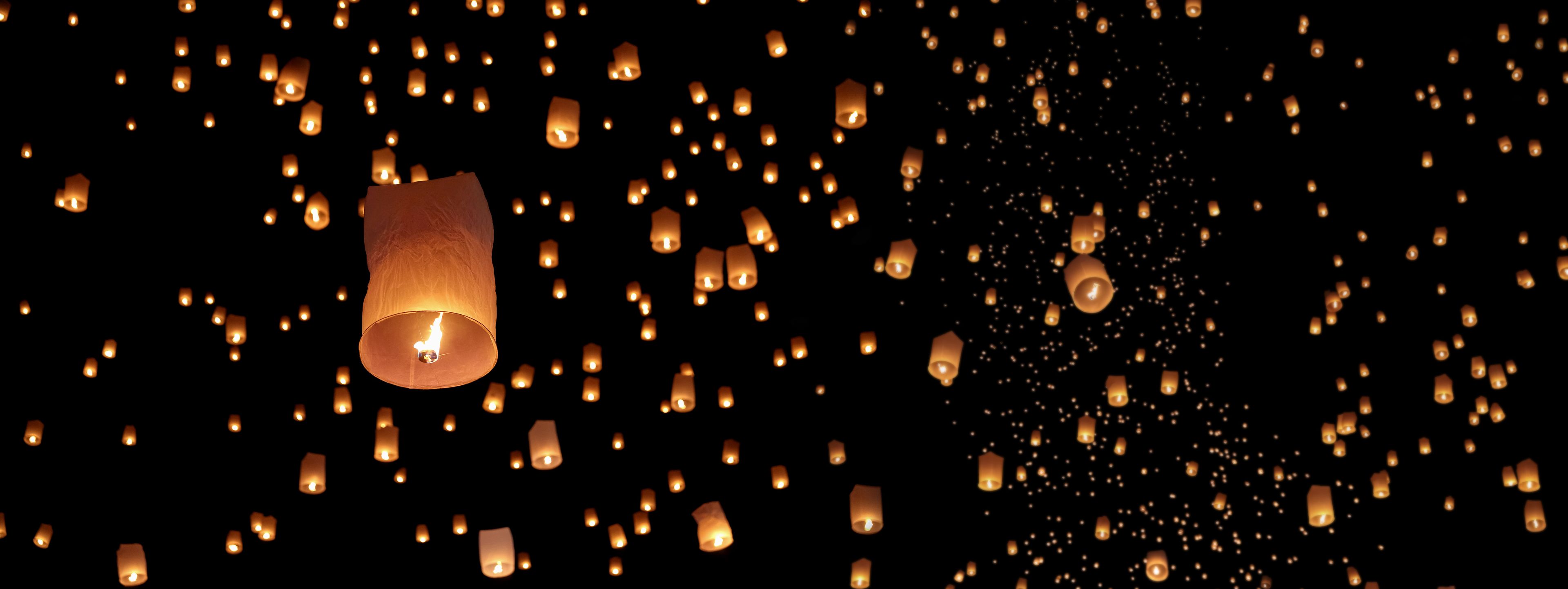 De nombreuses lanternes volantes s'élèvent dans le ciel sombre de la nuit.
