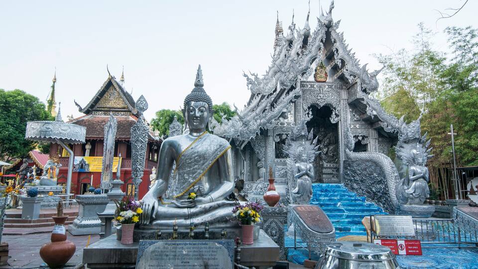 A large Buddha statue in front of a temple with intricate architecture and a dragon statue.