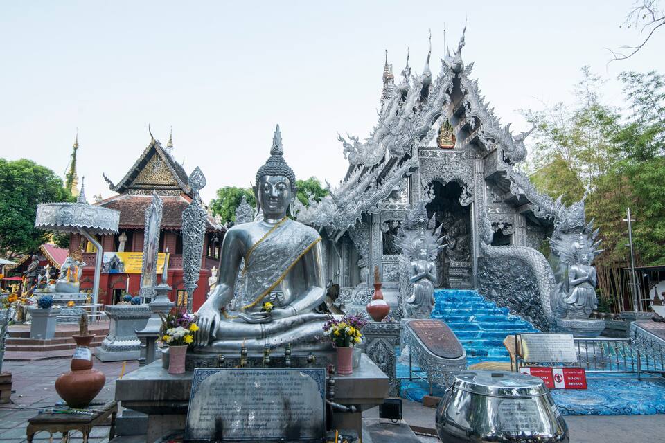 Uma grande estátua de Buda em frente a um templo com arquitetura elaborada e uma estátua de dragão.