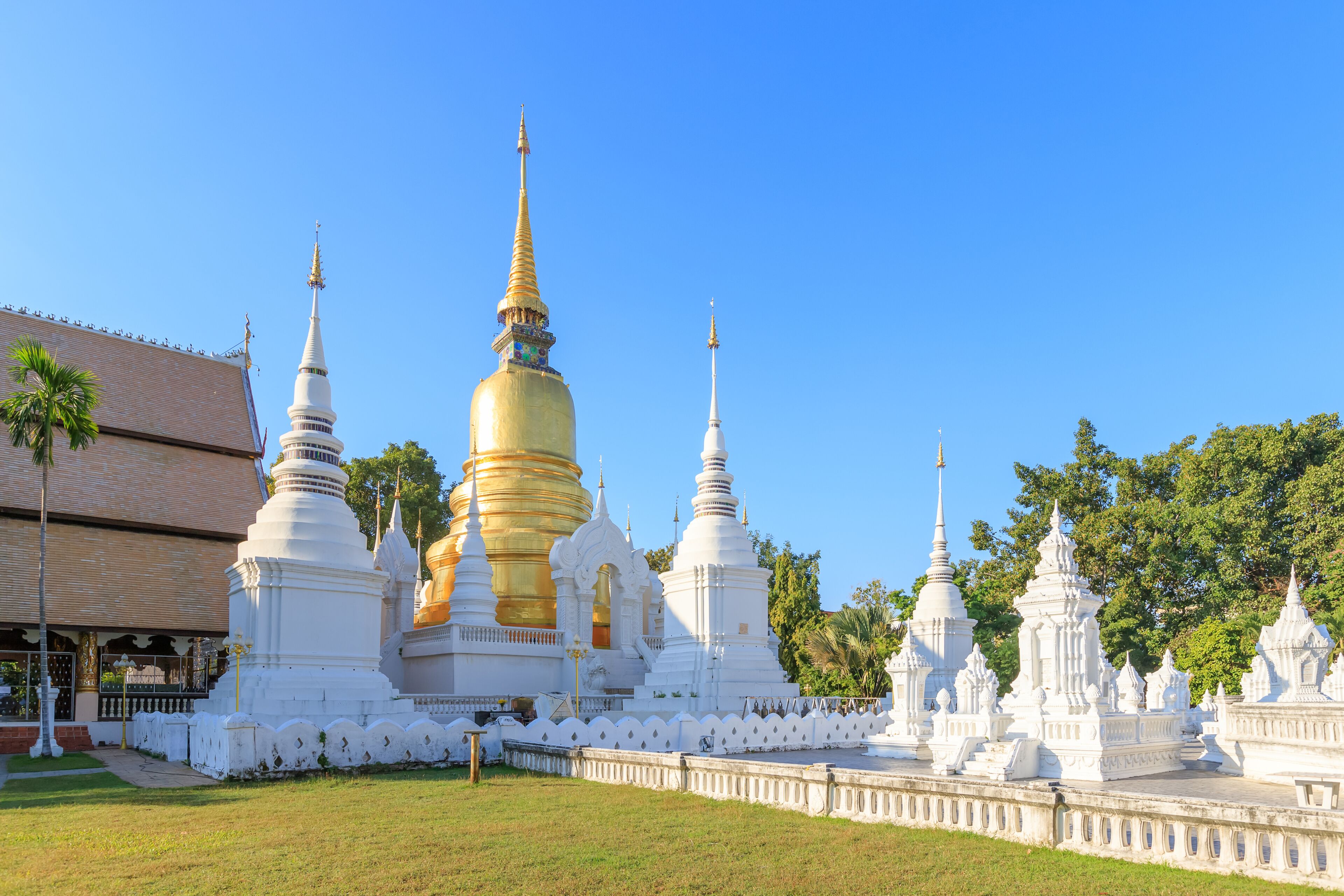A temple complex with golden and white stupas, surrounded by a white fence, under a clear blue sky.