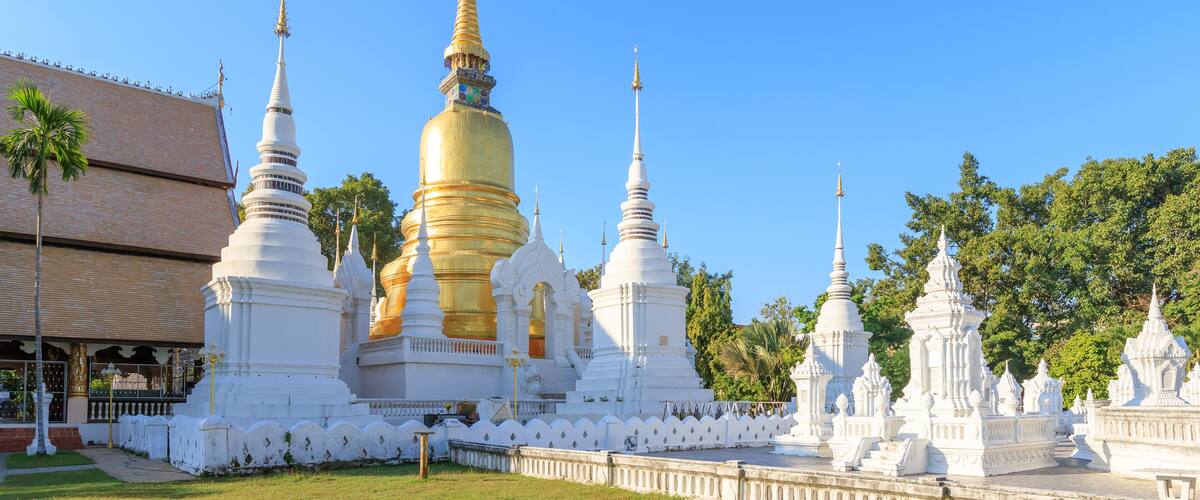 A temple complex with golden and white stupas, surrounded by a white fence, under a clear blue sky.