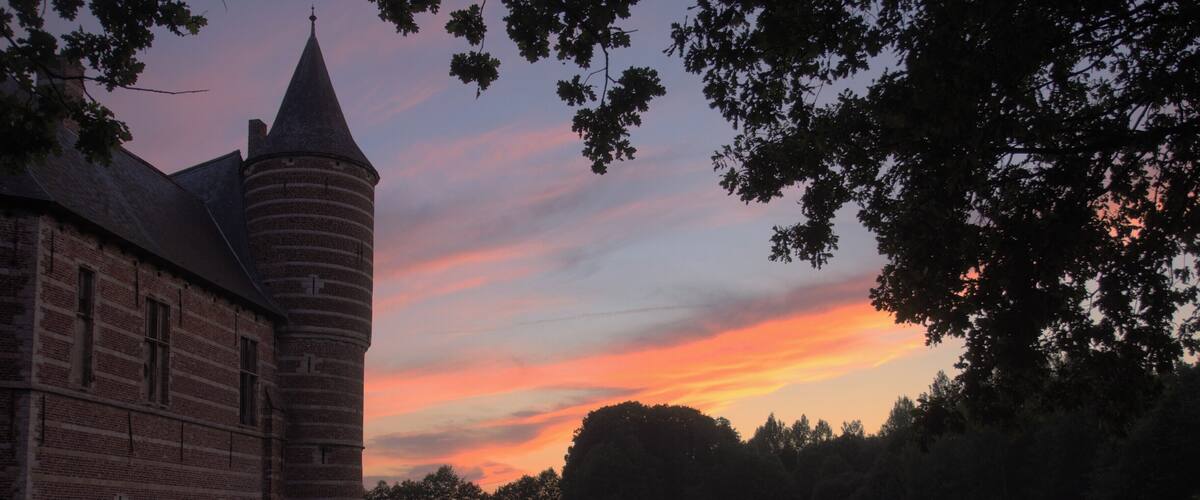 A brick building with a tower, a calm lake, and a sunset sky.