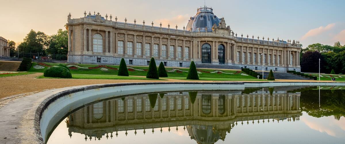 A grand building with a dome and columns, surrounded by a reflective pool and trimmed hedges.