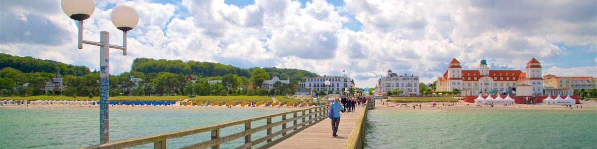 Eine Holzstege, der sich in ein türkisfarbenes Meer erstreckt, mit blauem Himmel und Gebäuden im Hintergrund.