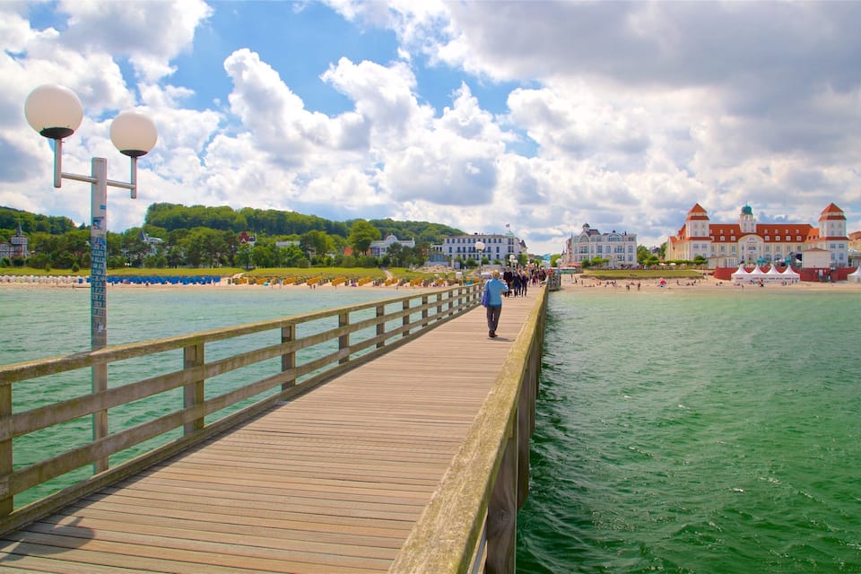 A wooden pier extending into a turquoise sea, with a clear sky and buildings in the background.