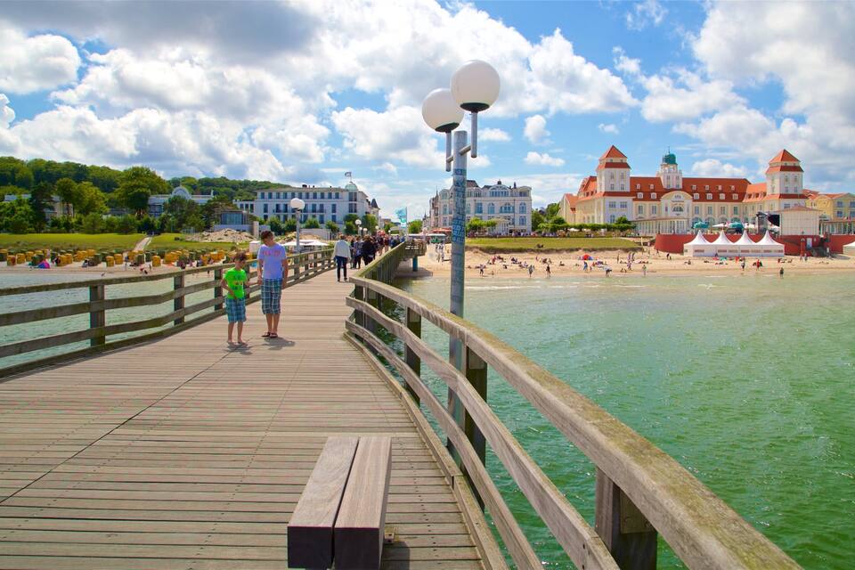 A wooden boardwalk along a beach with people walking, a large building with a tower, and a clear sky.