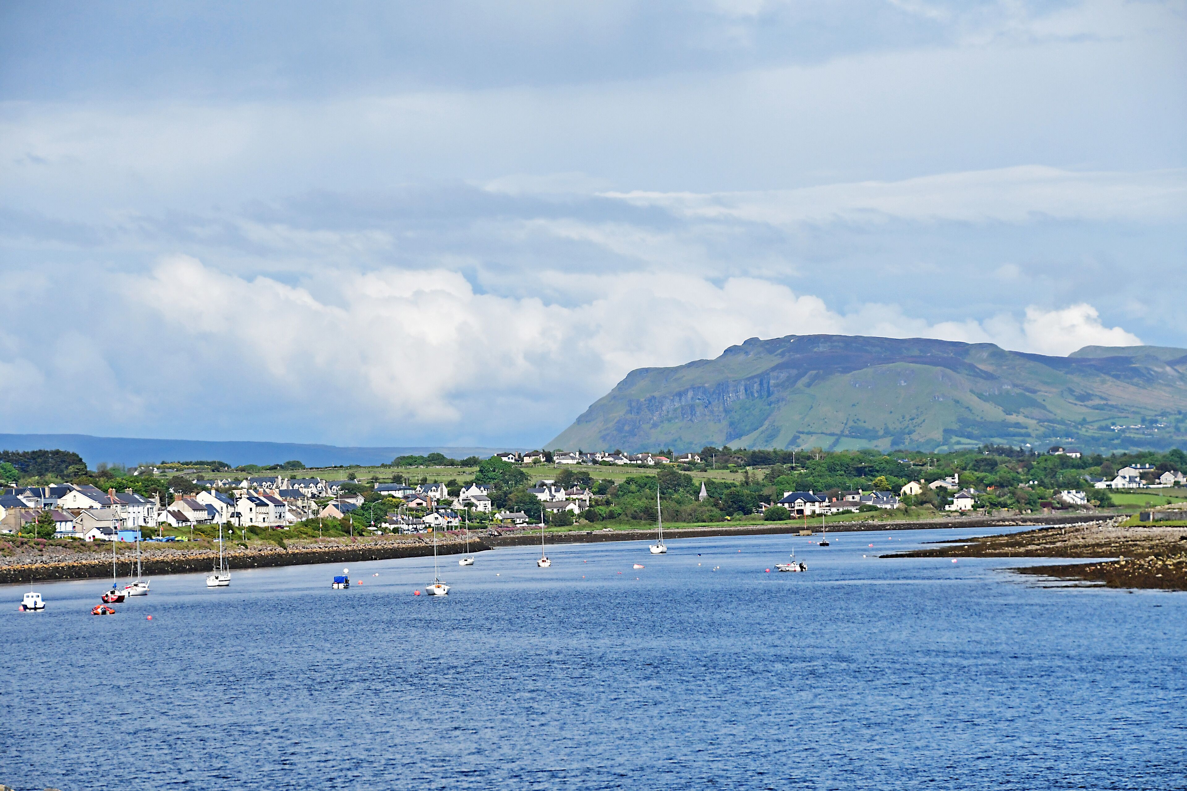 A coastal town with houses, sailboats, and a mountain in the background.