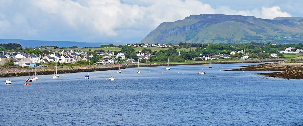 A coastal town with houses, sailboats, and a mountain in the background.