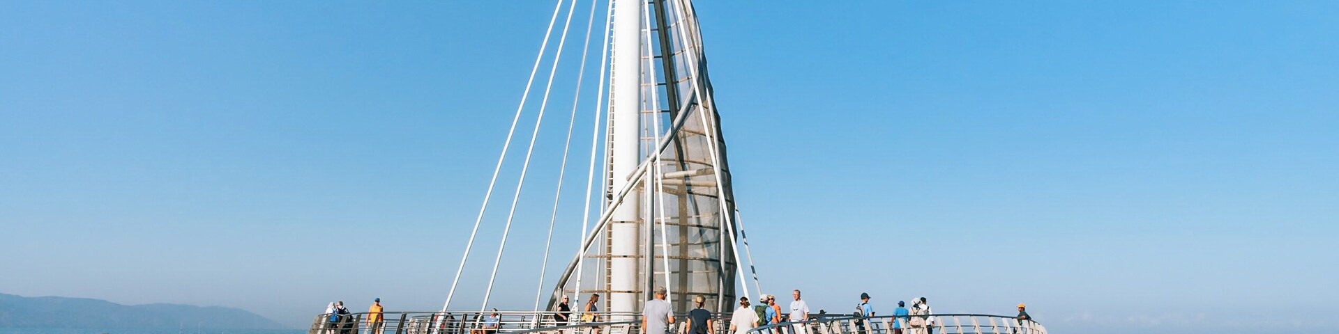 A cable-stayed bridge with a central tower, pedestrian walkway, and boats in the water.