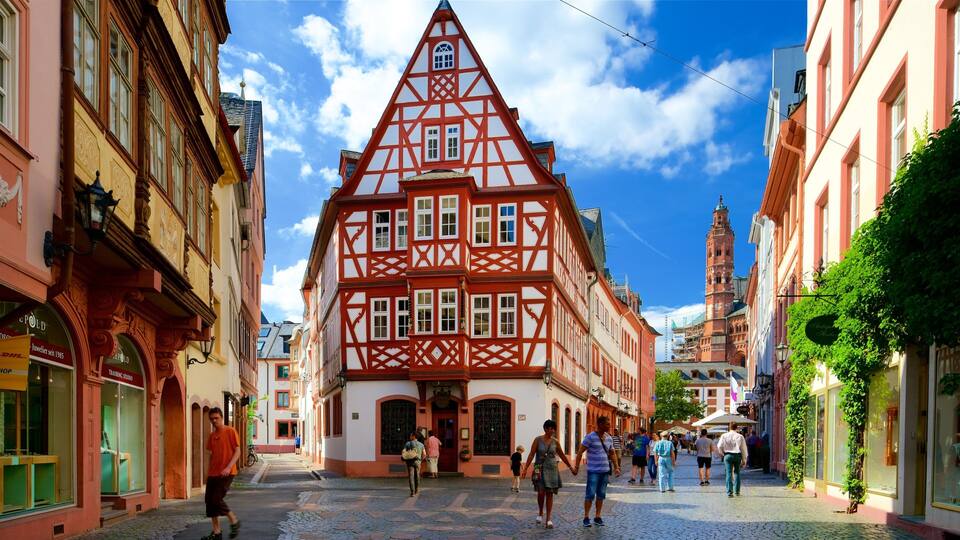 A cobblestone street lined with traditional half-timbered houses, a prominent tower, and pedestrians.