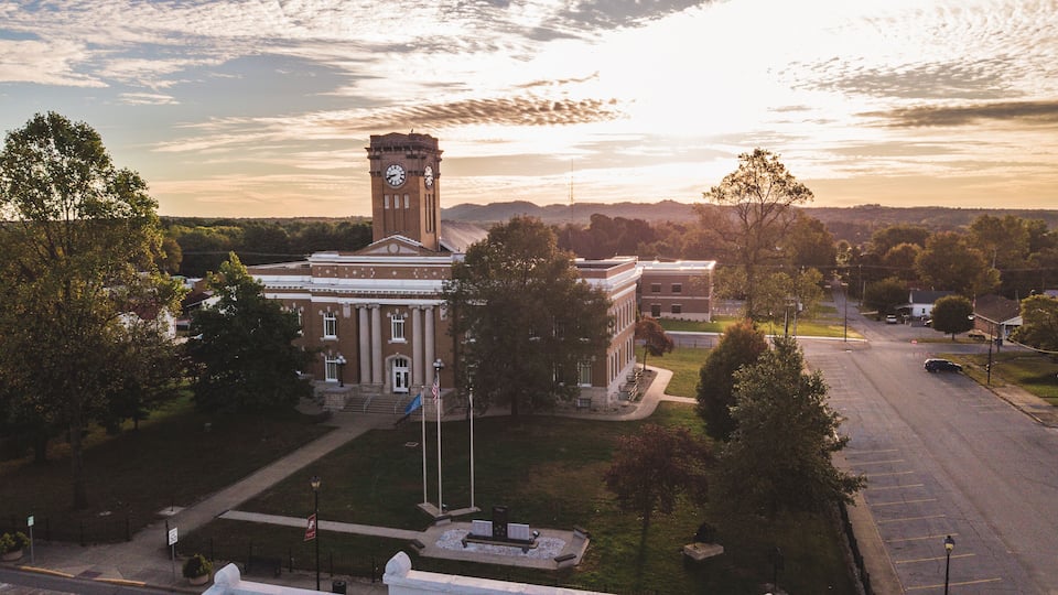 A courthouse with a clock tower, surrounded by trees and a parking lot.