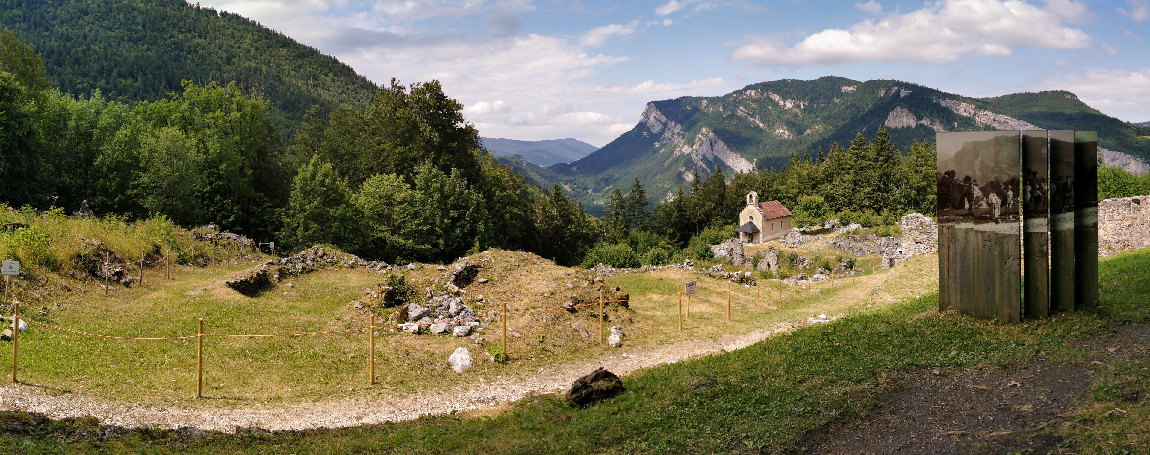 A mountainous landscape with a church, a wooden structure, and a fenced area.