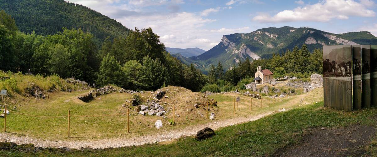 A mountainous landscape with a church, a wooden structure, and a fenced area.