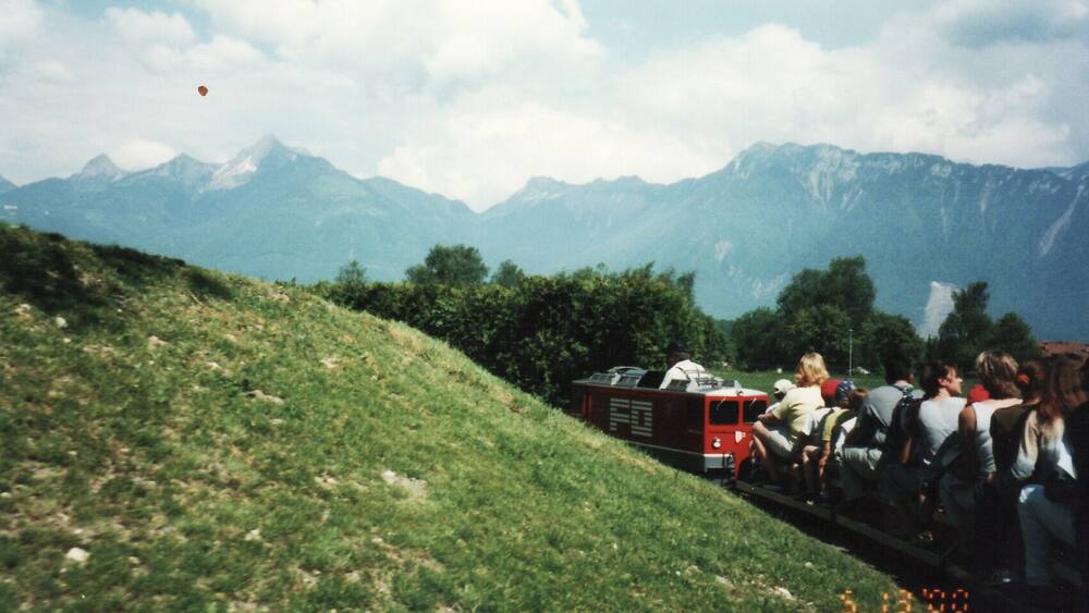 Ein rotes Fahrzeug auf einer grasbewachsenen Böschung, im Hintergrund Berge.
