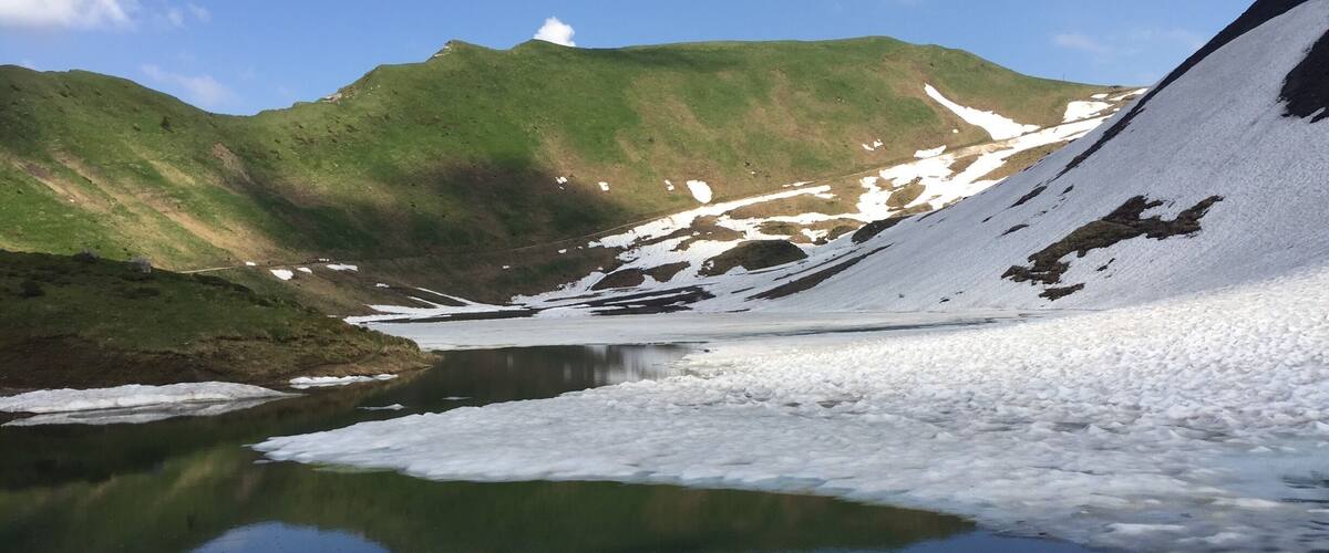 A glacial lake surrounded by snow-covered mountains and green hills.