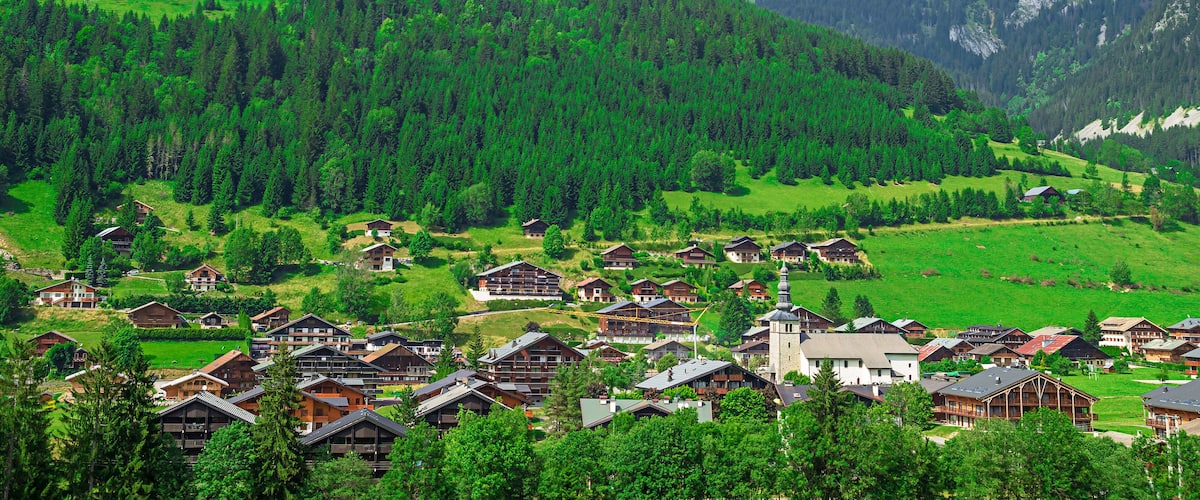 A mountainous village with wooden houses nestled among lush green hills and dense forests.