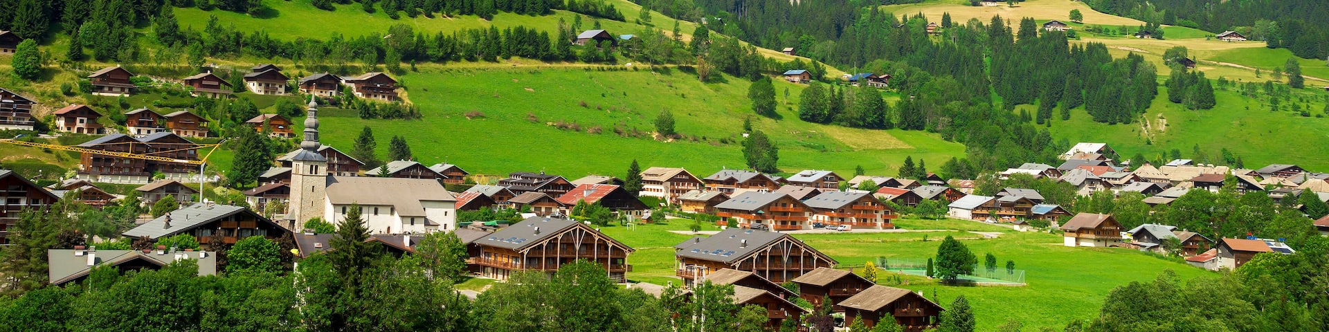 A mountainous village with wooden houses, a church, and green fields.