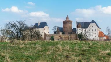 A historic castle with a prominent tower, surrounded by a grassy field and trees.