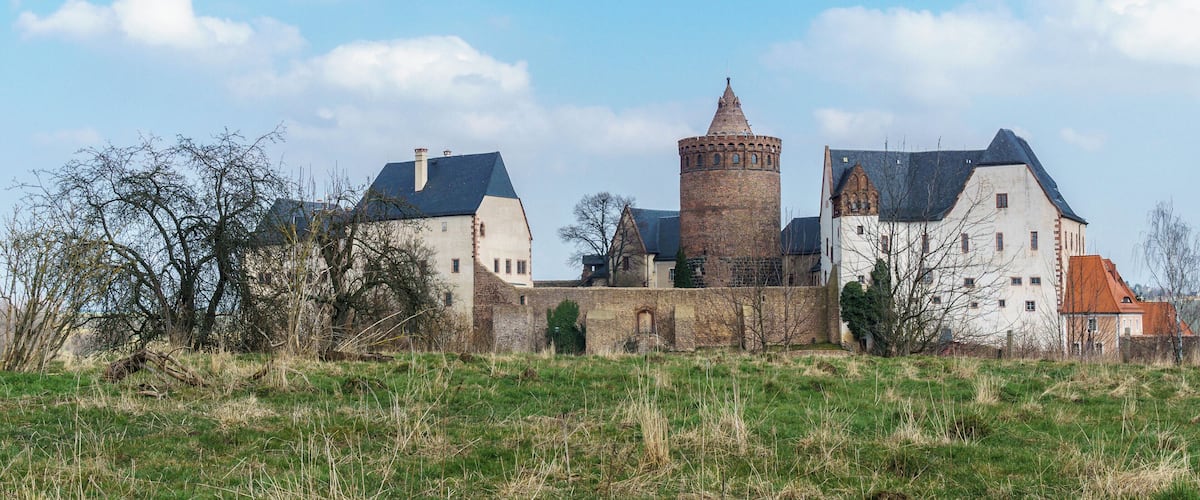 A historic castle with a prominent tower, surrounded by a grassy field and trees.
