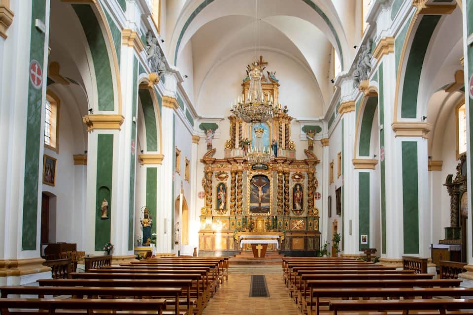 Interior ornamentado de una iglesia con un altar central, bancales y columnas verdes y blancas.