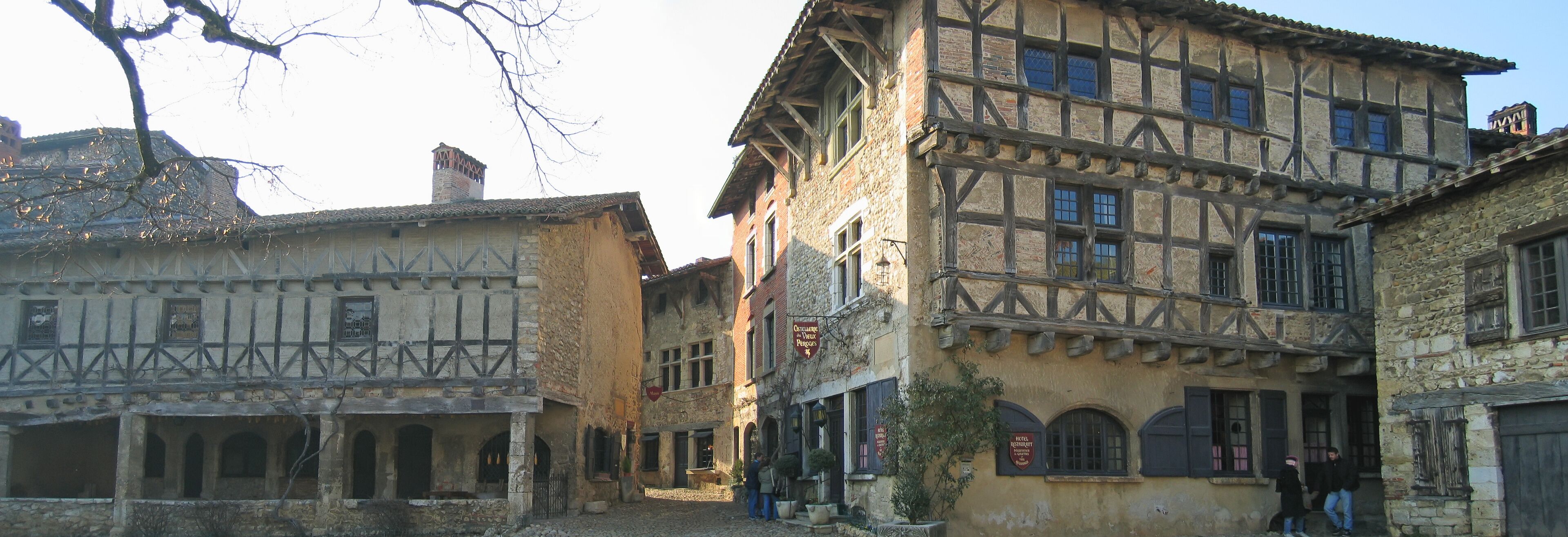 A narrow street with half-timbered buildings, cobblestone pavement, and a few pedestrians.