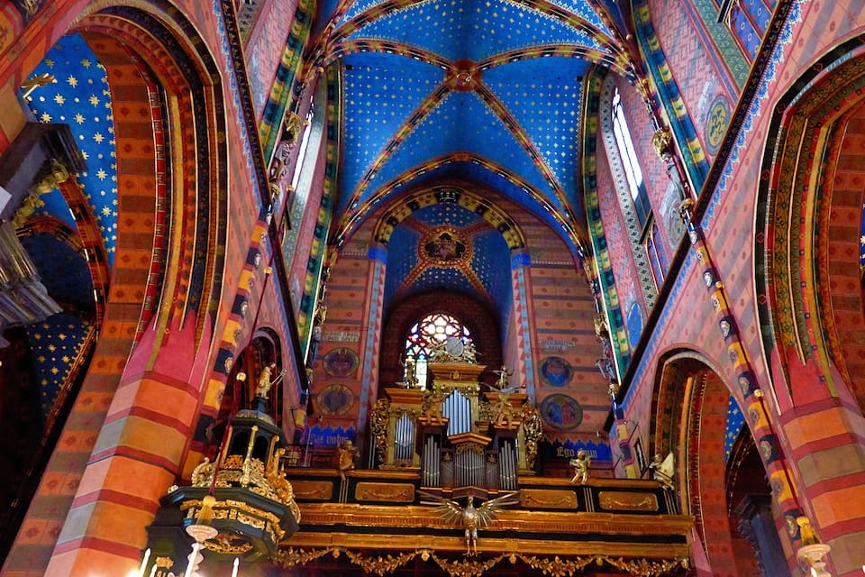 An ornate church interior with colorful stained glass windows, intricate ceiling designs, and a central altar.