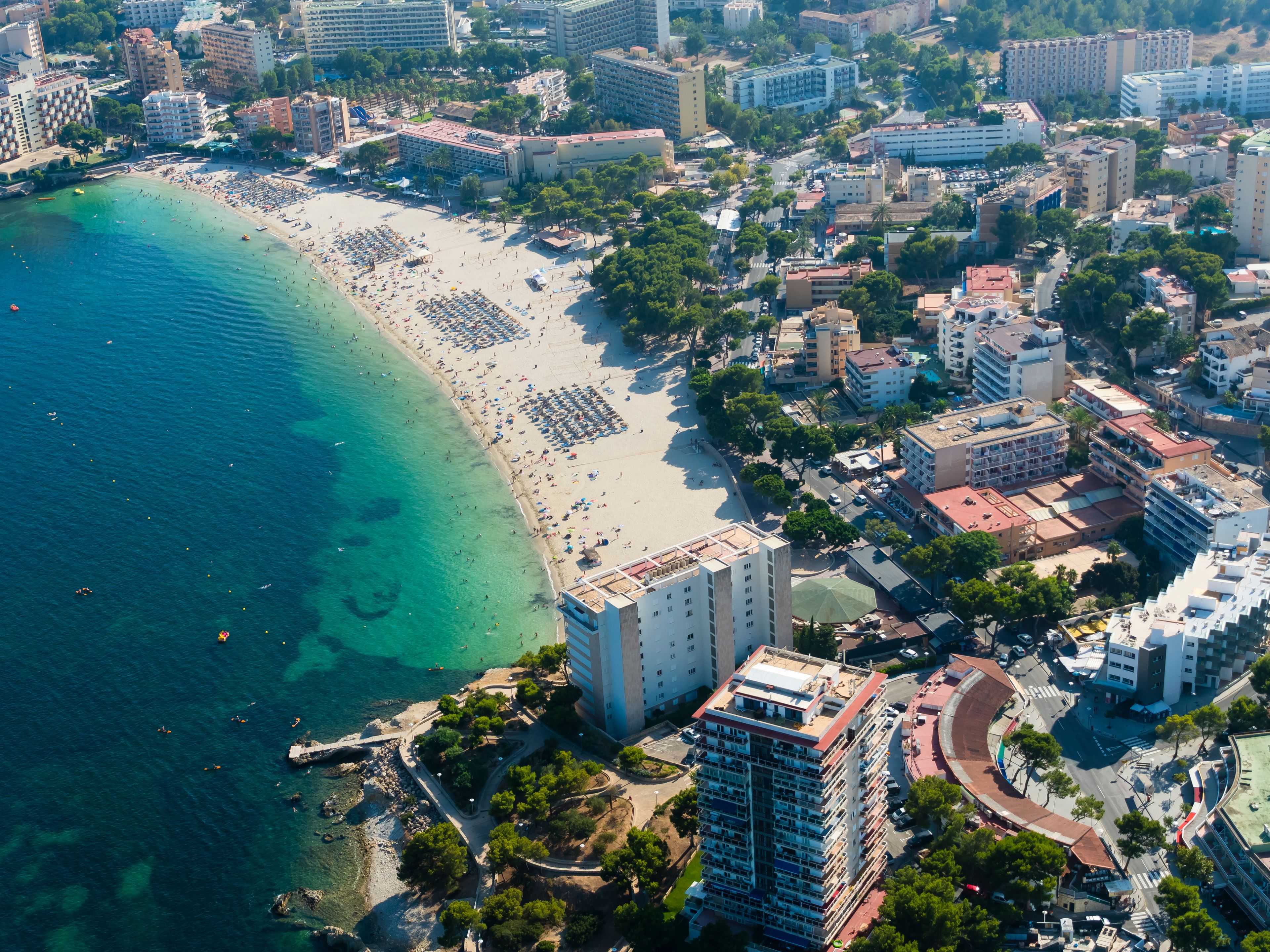 Vista aérea de una ciudad costera con playa, edificios y un mar azul cristalino.