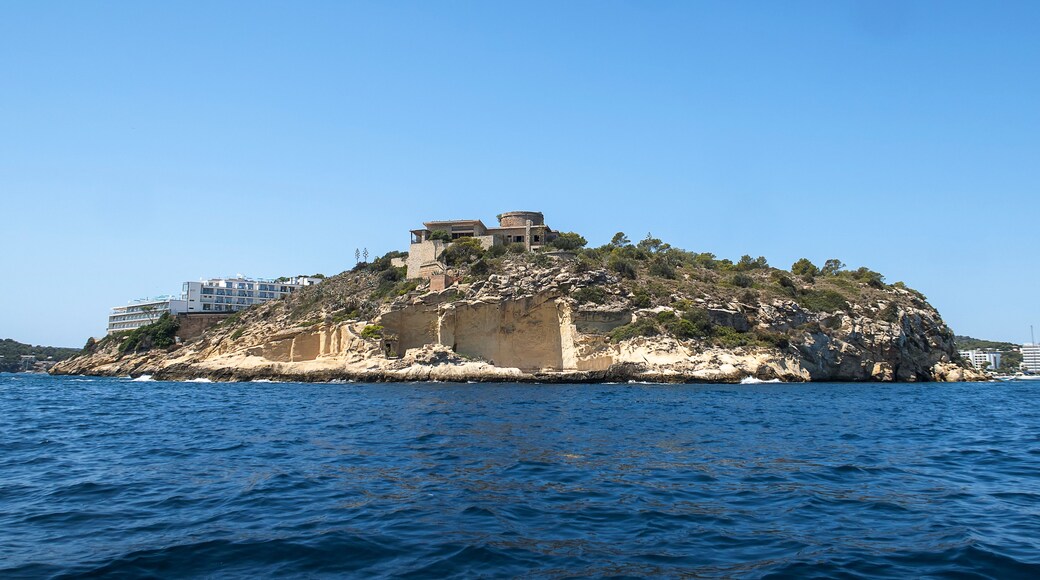 A rocky island with buildings on top, surrounded by clear blue water.
