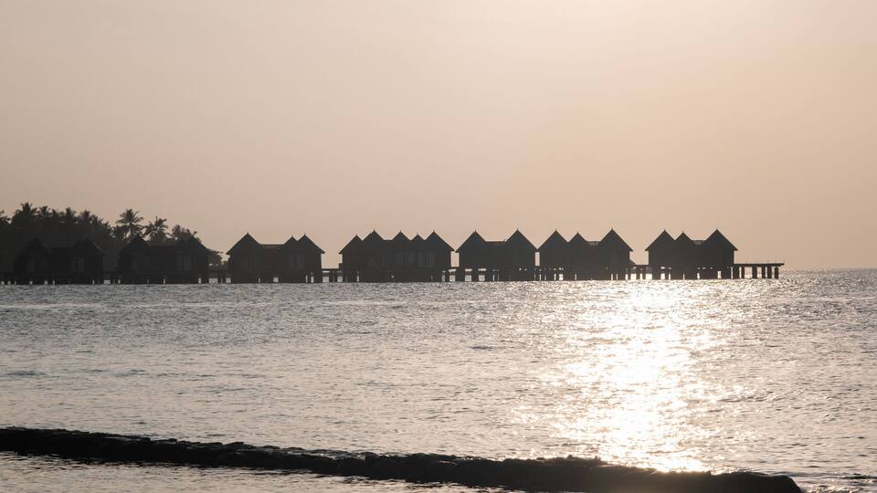 A row of overwater bungalows silhouetted against a sunset.