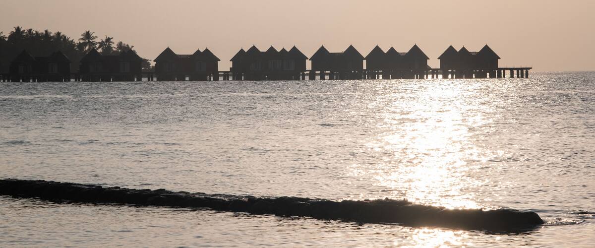 A row of overwater bungalows silhouetted against a sunset.