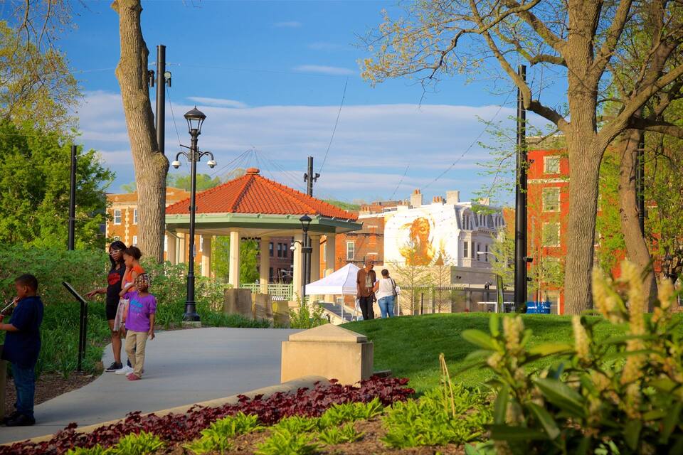 A park with a gazebo, trees, and a red-roofed building in the background.