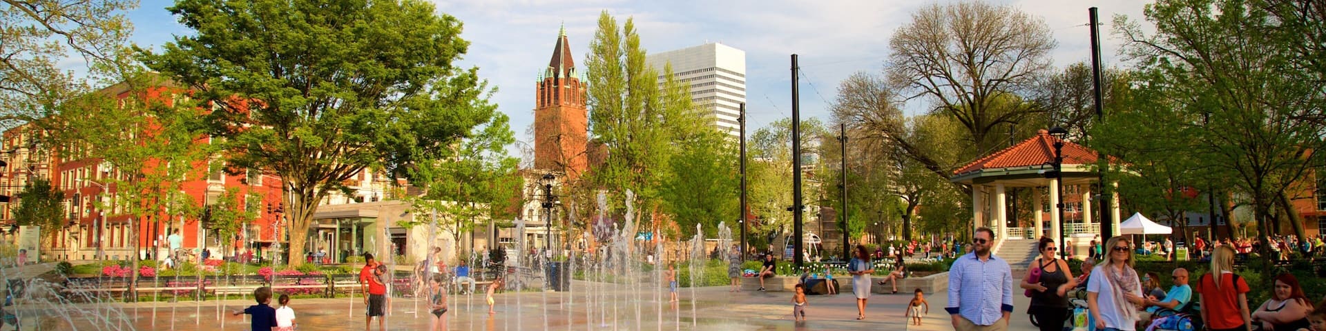 A public square with a water fountain, trees, and a gazebo.