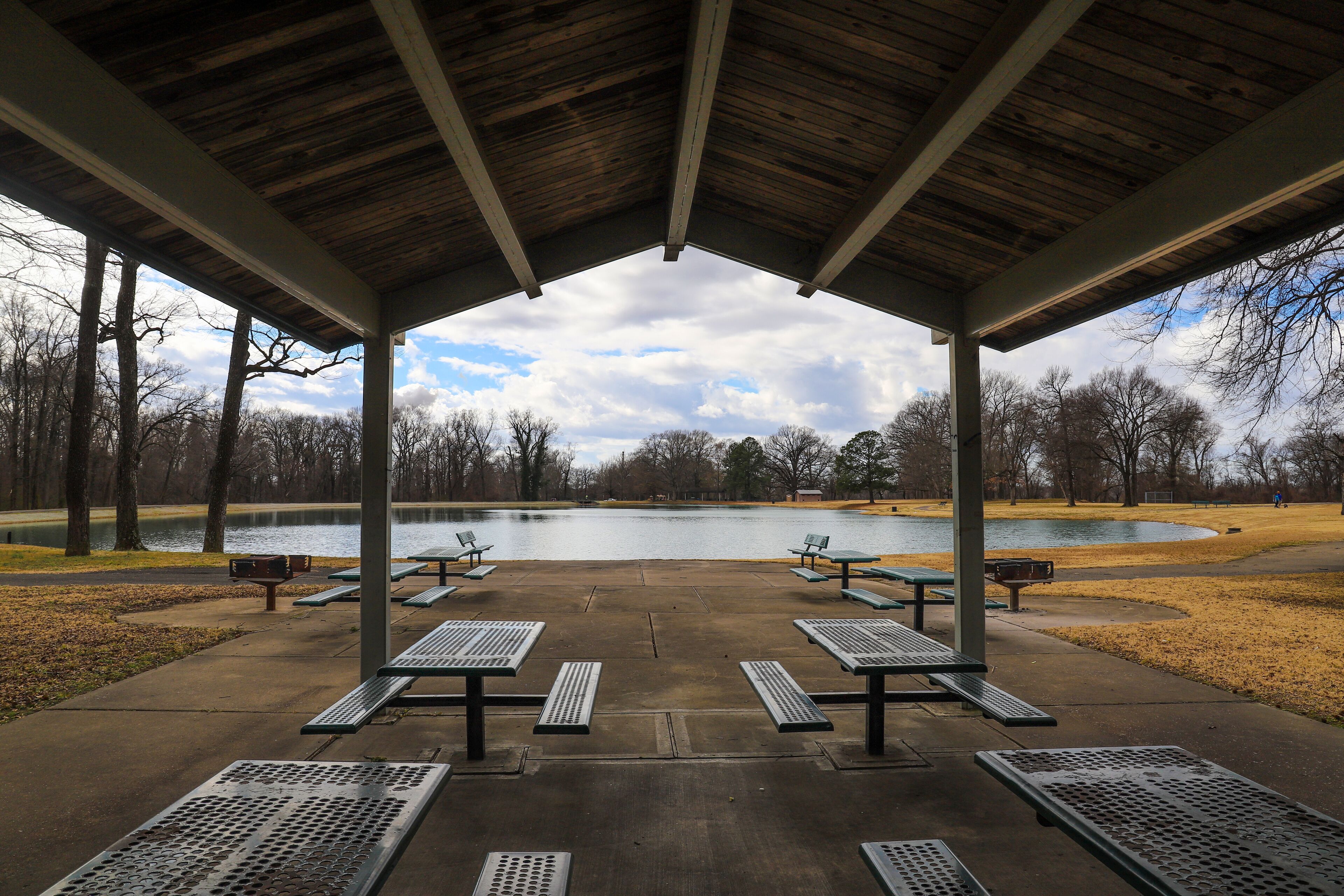a wooden pergola near a still green lake with green metal park benches underneath surrounded by bare winter trees and yellow winter grass at Martin Luther King, Jr. Riverside Park in Memphis Tennessee