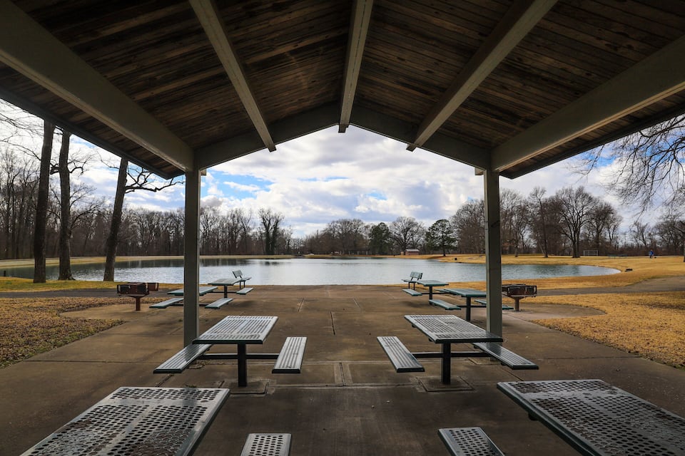 A covered picnic area with benches and a lake in the background.