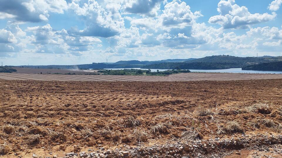 A vast, dry landscape with a distant lake and hills under a partly cloudy sky.