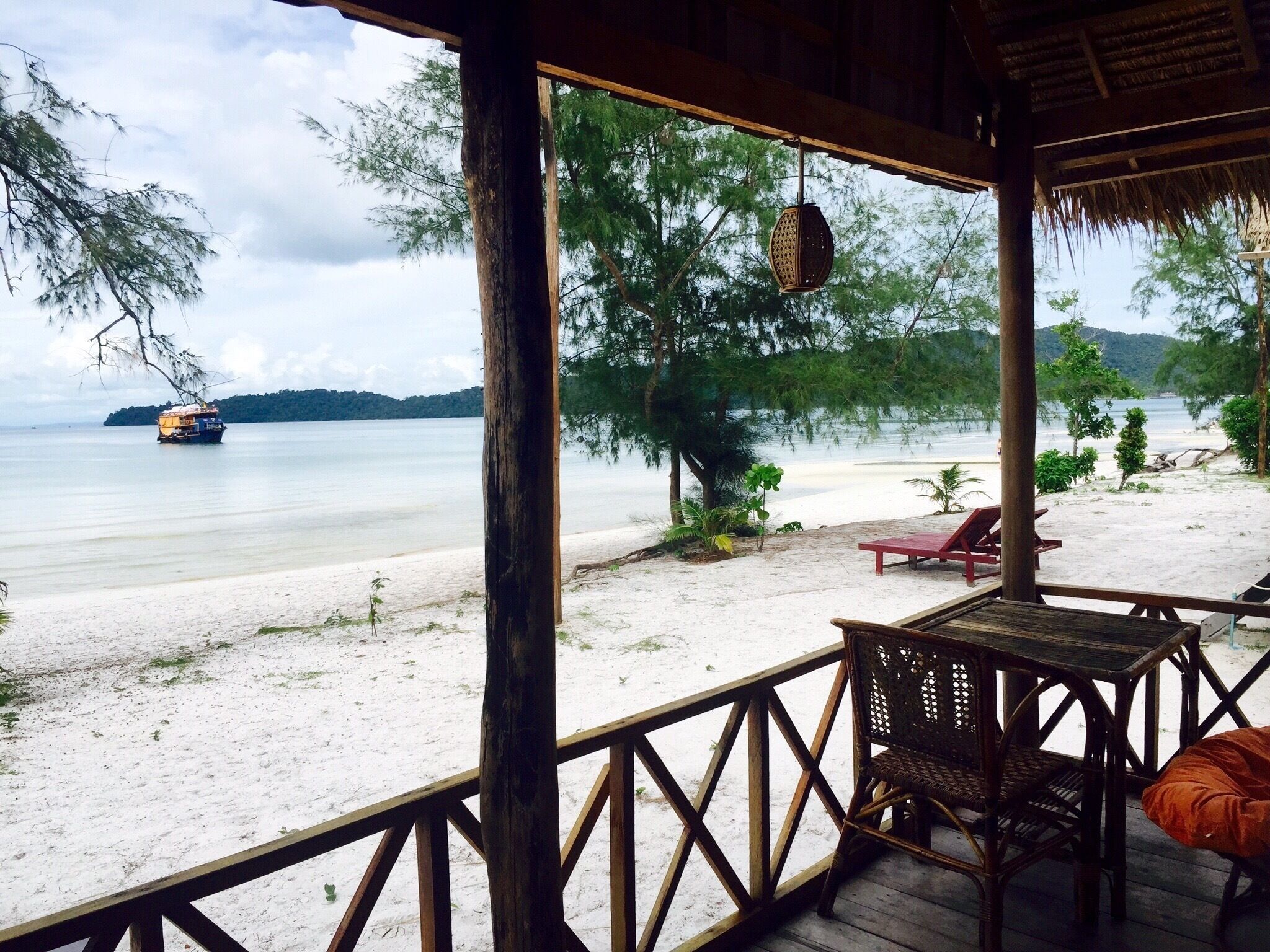 A wooden deck overlooking a beach with a boat in the distance.