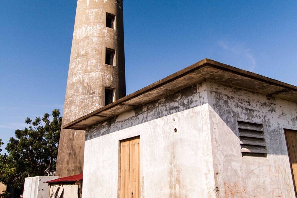 Um farol desgastado pelo tempo, com uma torre cilíndrica e um edifício menor anexo.